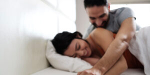 Young couple engaging in playful pillow fight on bed, smiling and enjoying each other's company, representing healthy relationships, intimacy, and emotional connection.