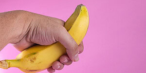 Banana held in hand against pink background, symbolizing health or nutrition concepts.